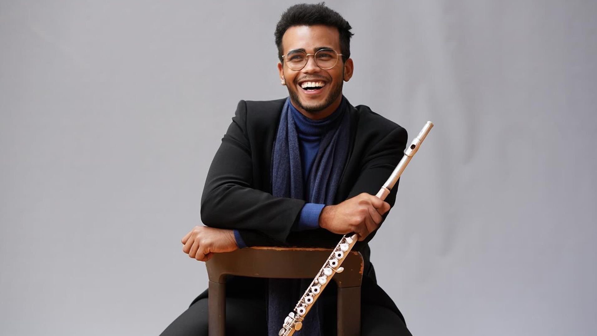 Javier Gutierrez sitzt mit einer Querflöte in der Hand auf einem Stuhl