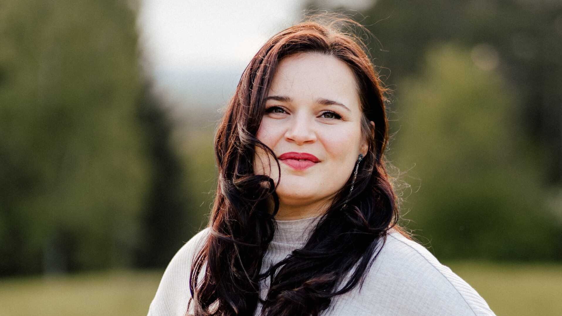 Lena Geiger in einem hellen Pullover mit verwehmte Haar in der Natur