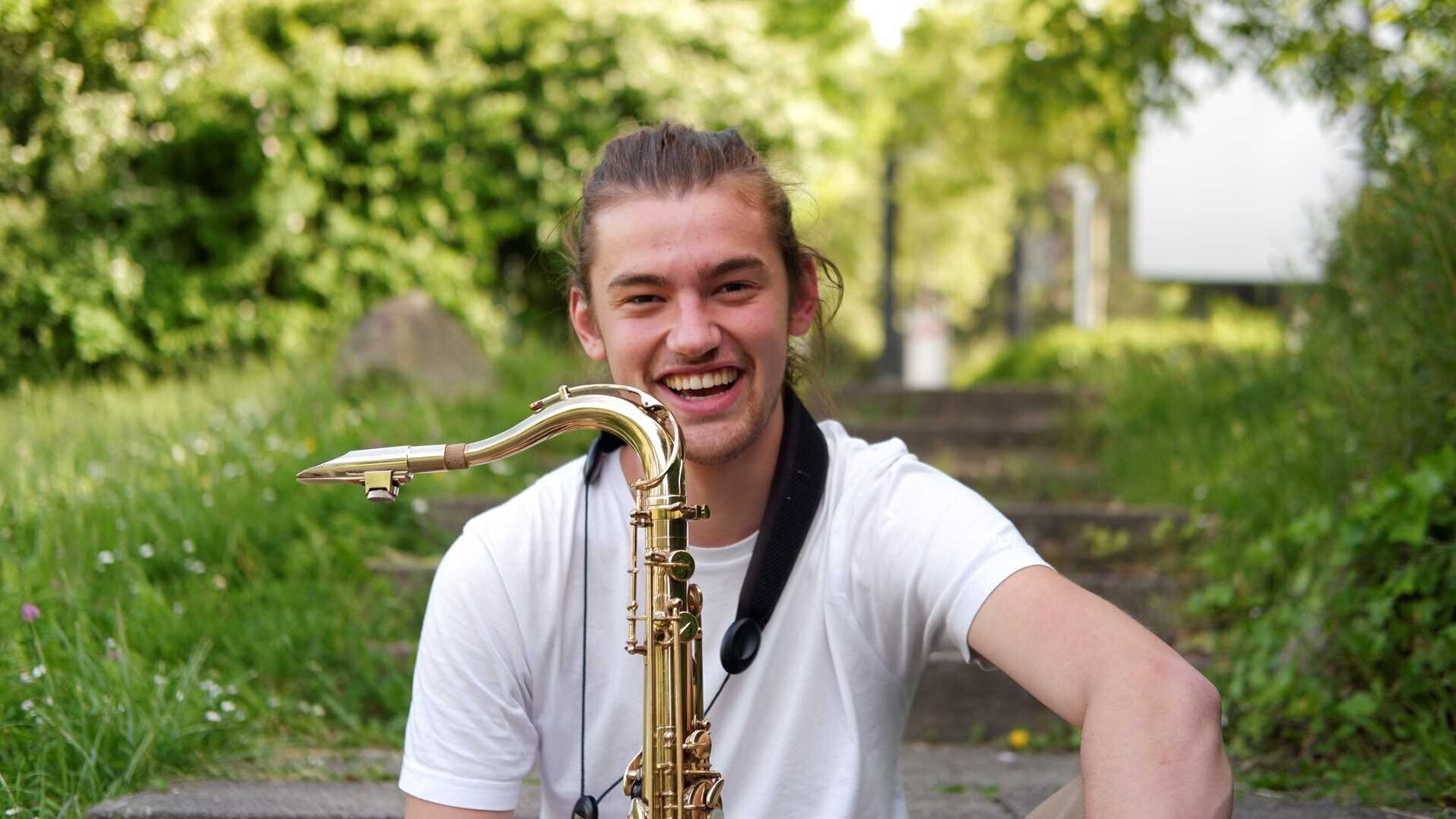 Theo Riethmüller sitzt mit Saxofon in der Hand in einem grünen Garten